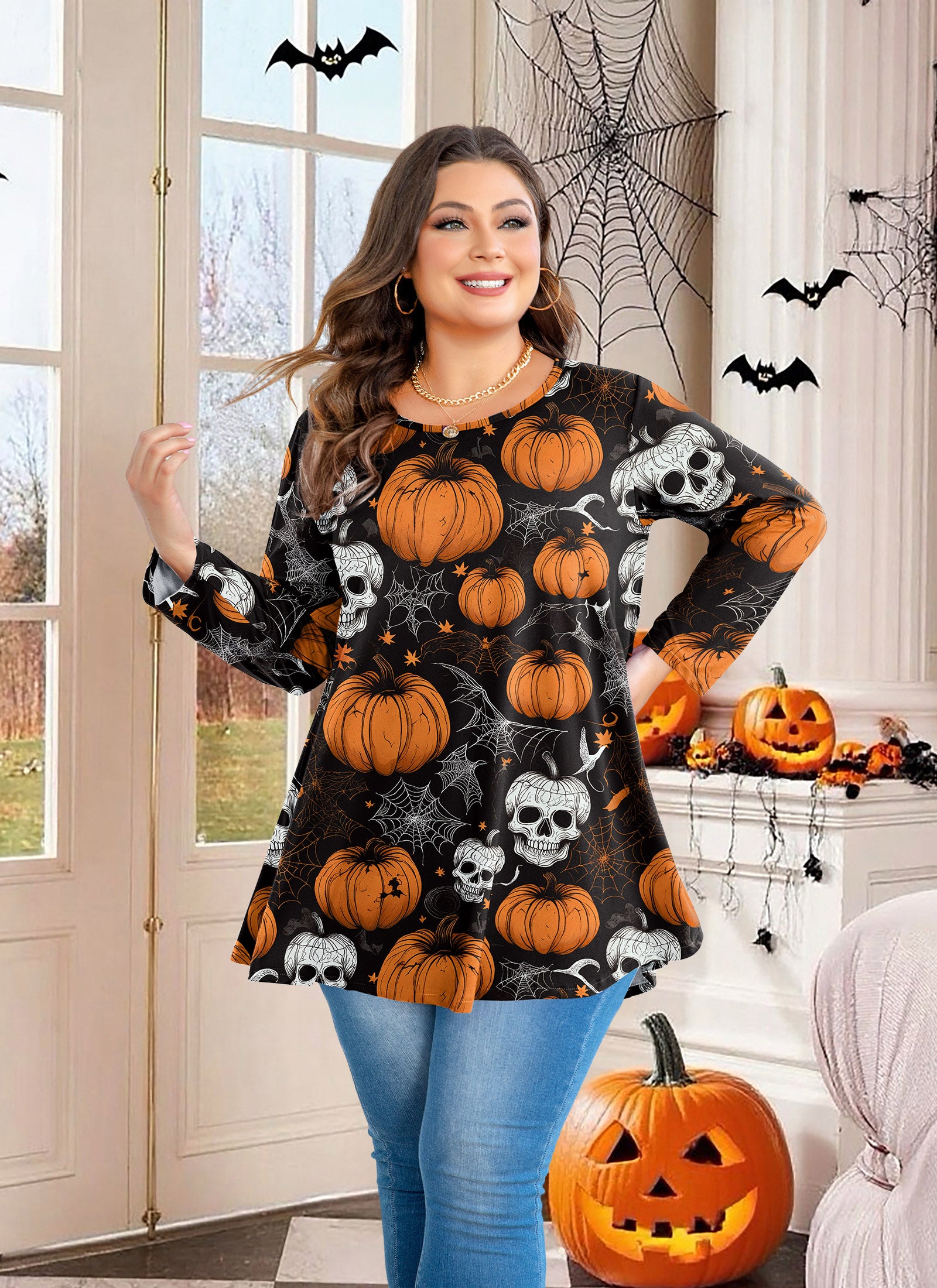 Woman wearing a Halloween-themed sweater with pumpkins and ghosts in a decorated room.