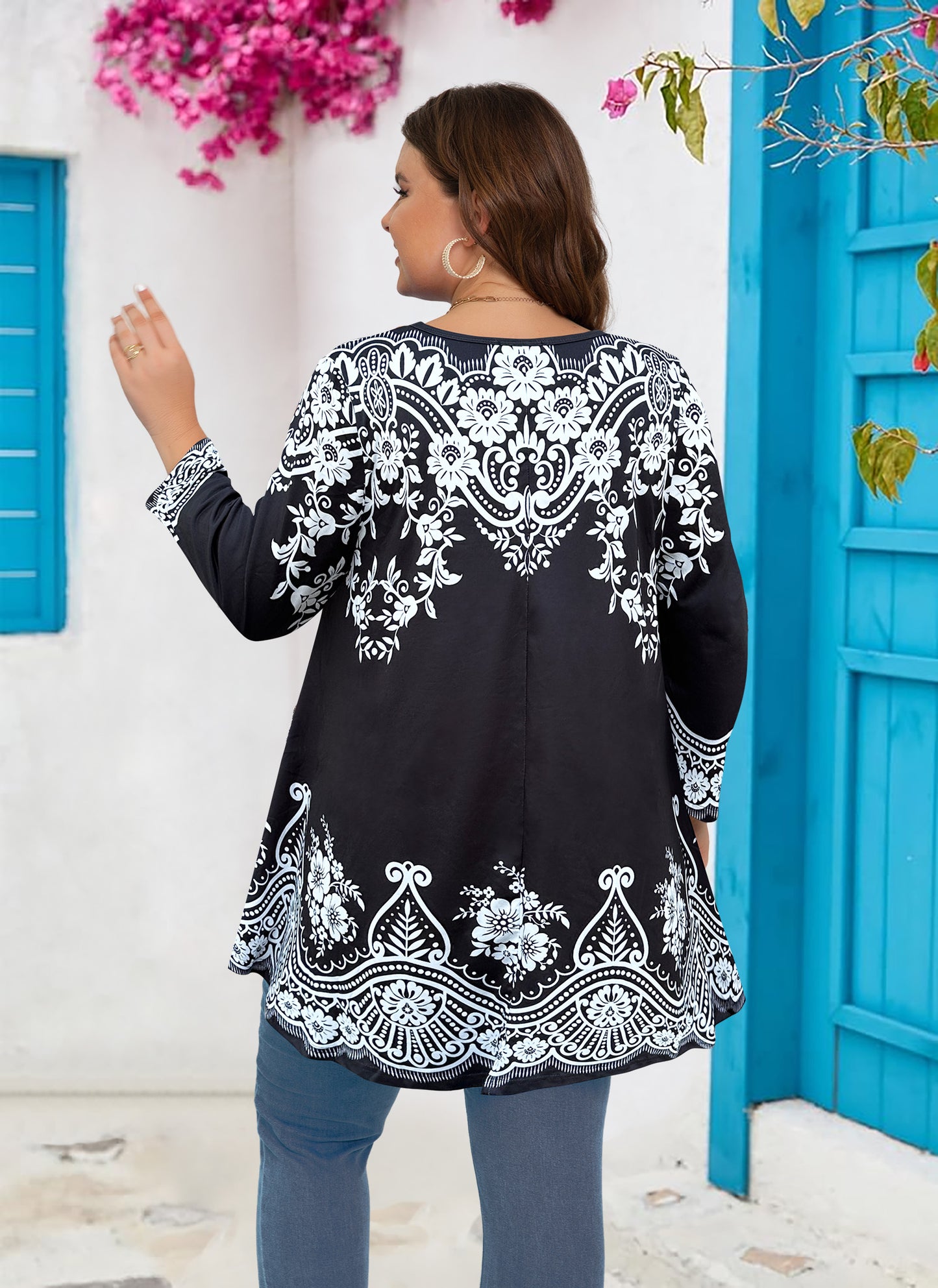 Woman wearing a black and white patterned top with a blue door and pink flowers in the background
