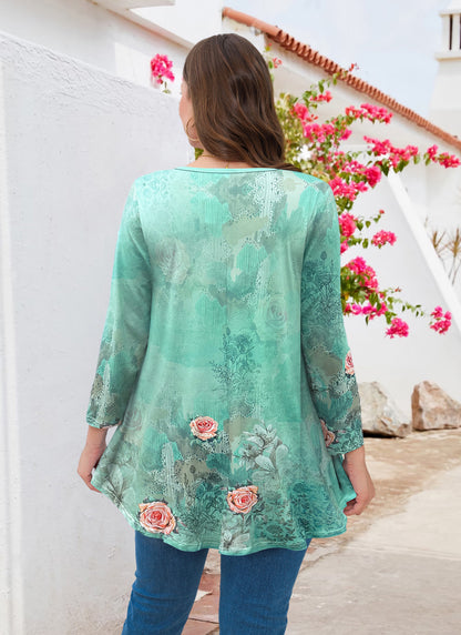 Woman wearing a green floral blouse standing in front of a white wall with pink flowers.